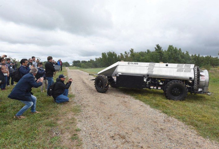 An unmanned spray vehicle travels through an orchard as onlookers record and photograph